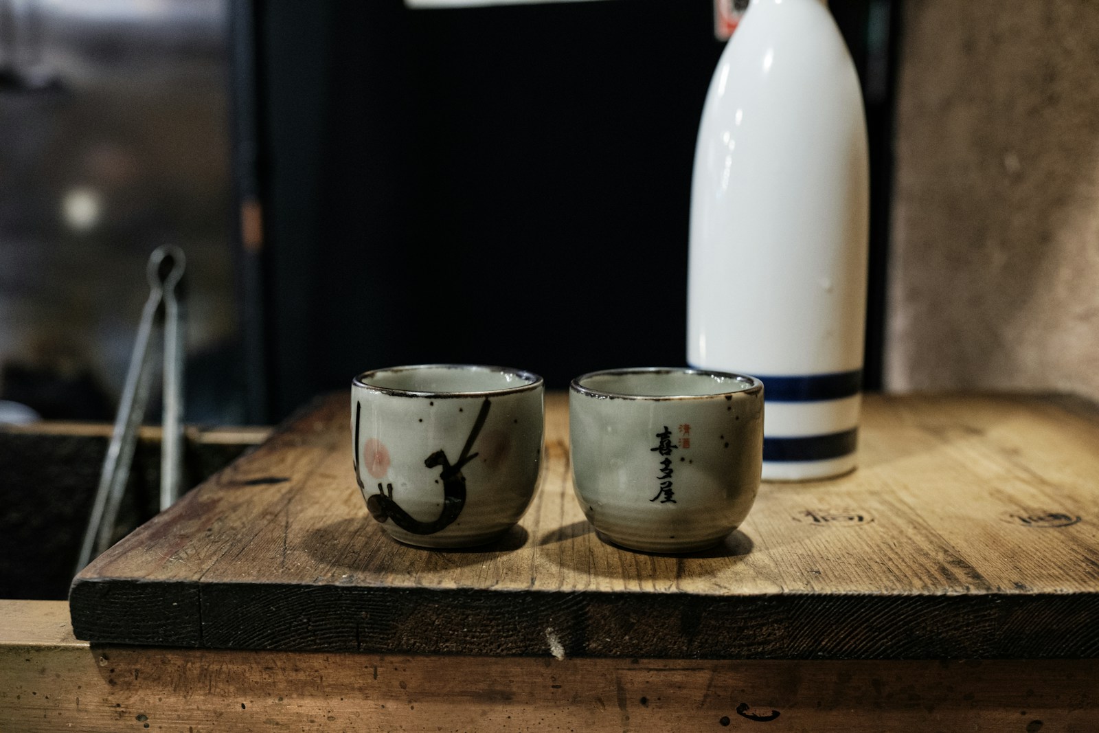徳利と2つのお猪口が木製のカウンターに並ぶ。日本酒の比較を象徴する一枚
